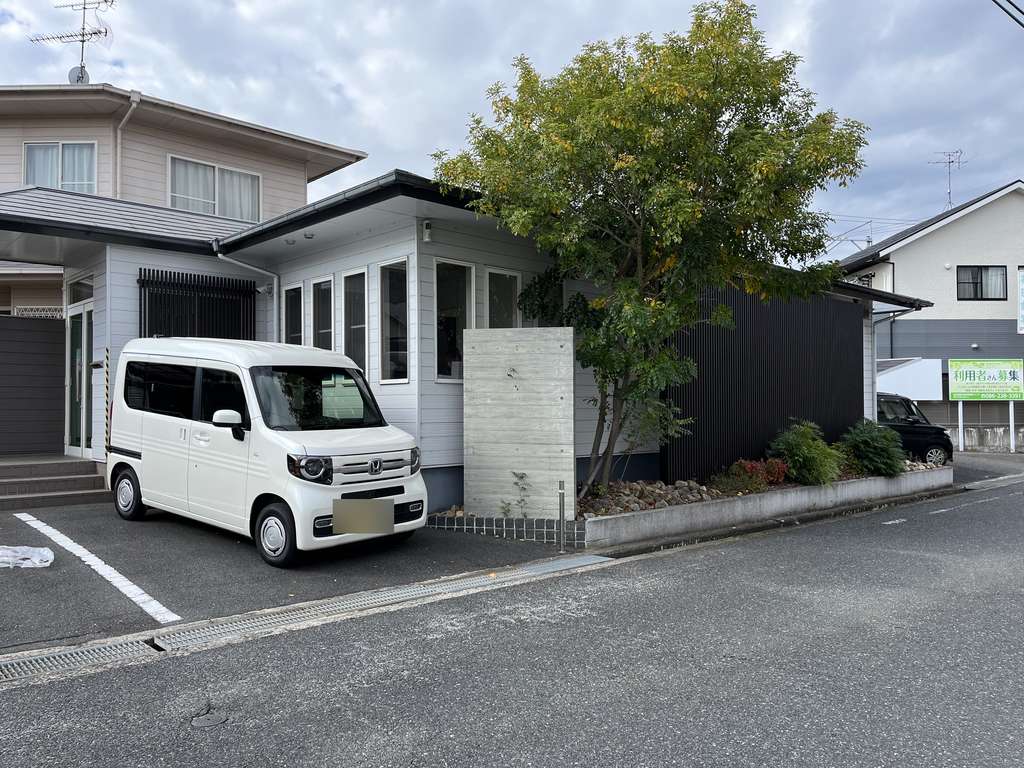 事業所の外観と、送迎に使う白い軽ワゴン車